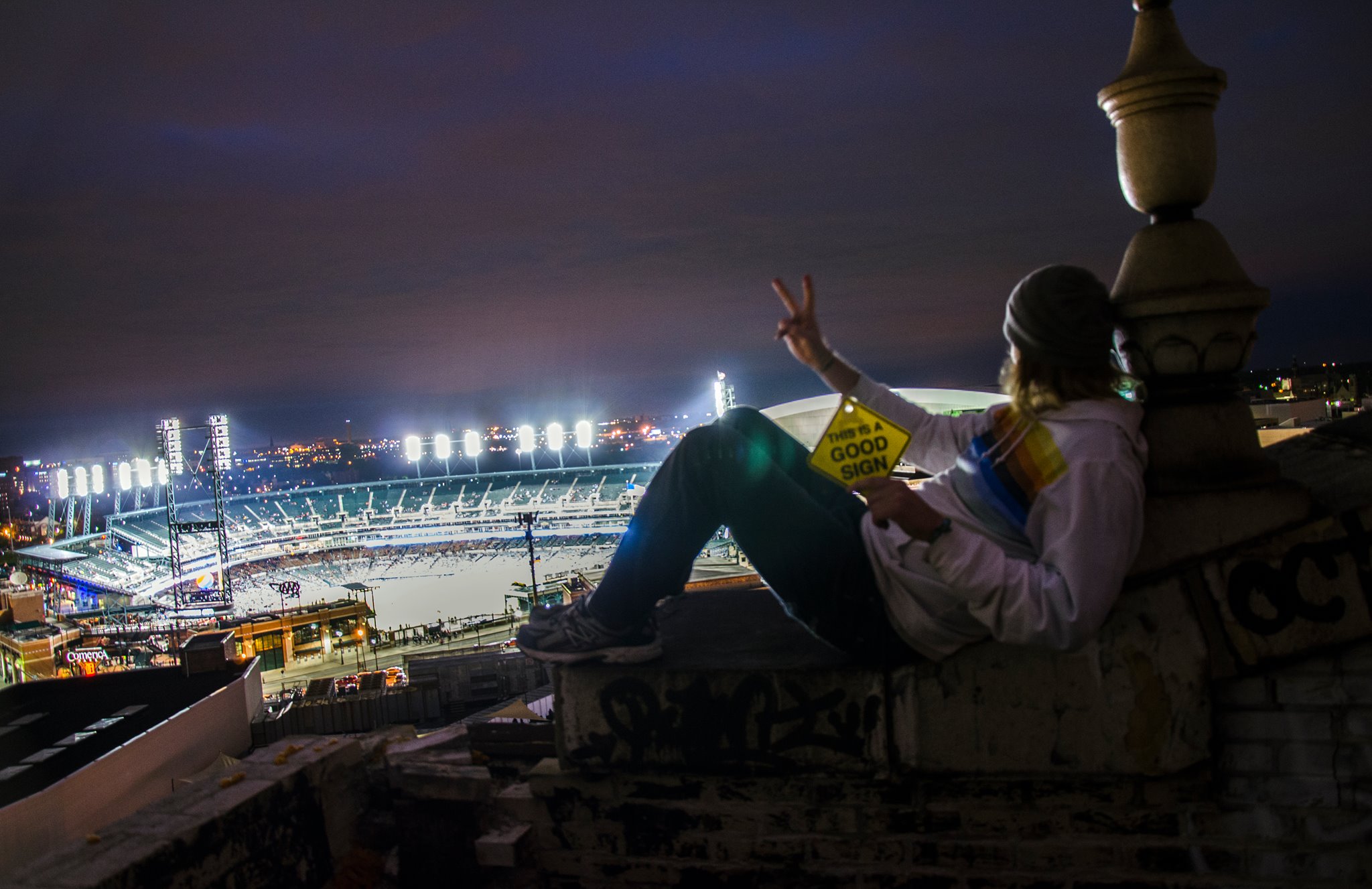 A person holding a Good Sign above a brightly lit festival venue at night